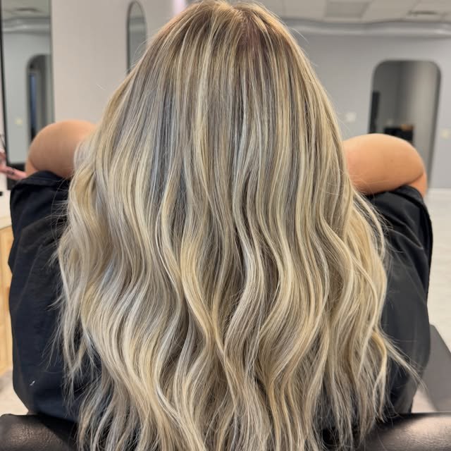 Bright blonde with a shadowed root, long layers finished in a soft wave.